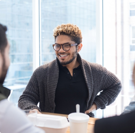 A man wearing a gray sweater sitting at a table having a conversation with peers