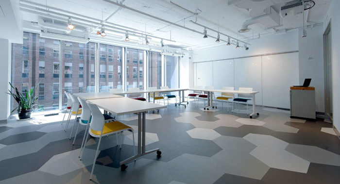 An empty meeting room with a hexagonal floor and white tables and chairs organized in a U shape