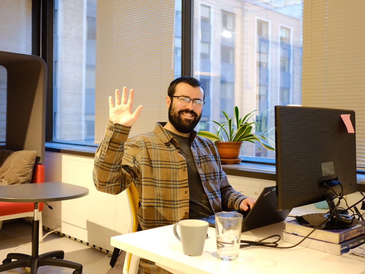 A man sitting at a computer waving at the camera