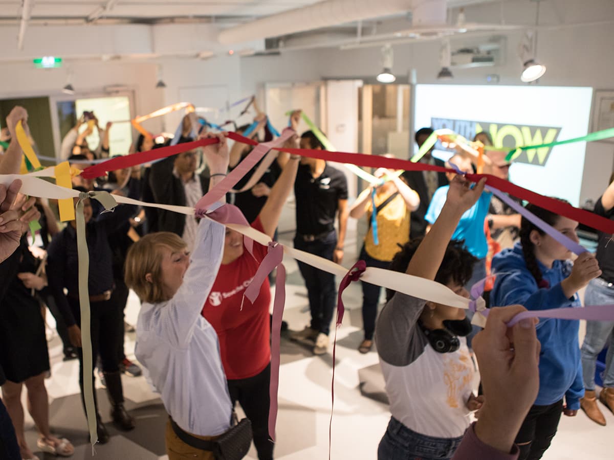 A group of people holding up a web of ribbons at Impact Hub Ottawa
