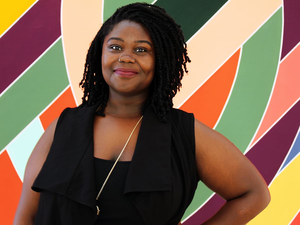 A Black woman standing in front of a multi-coloured wall