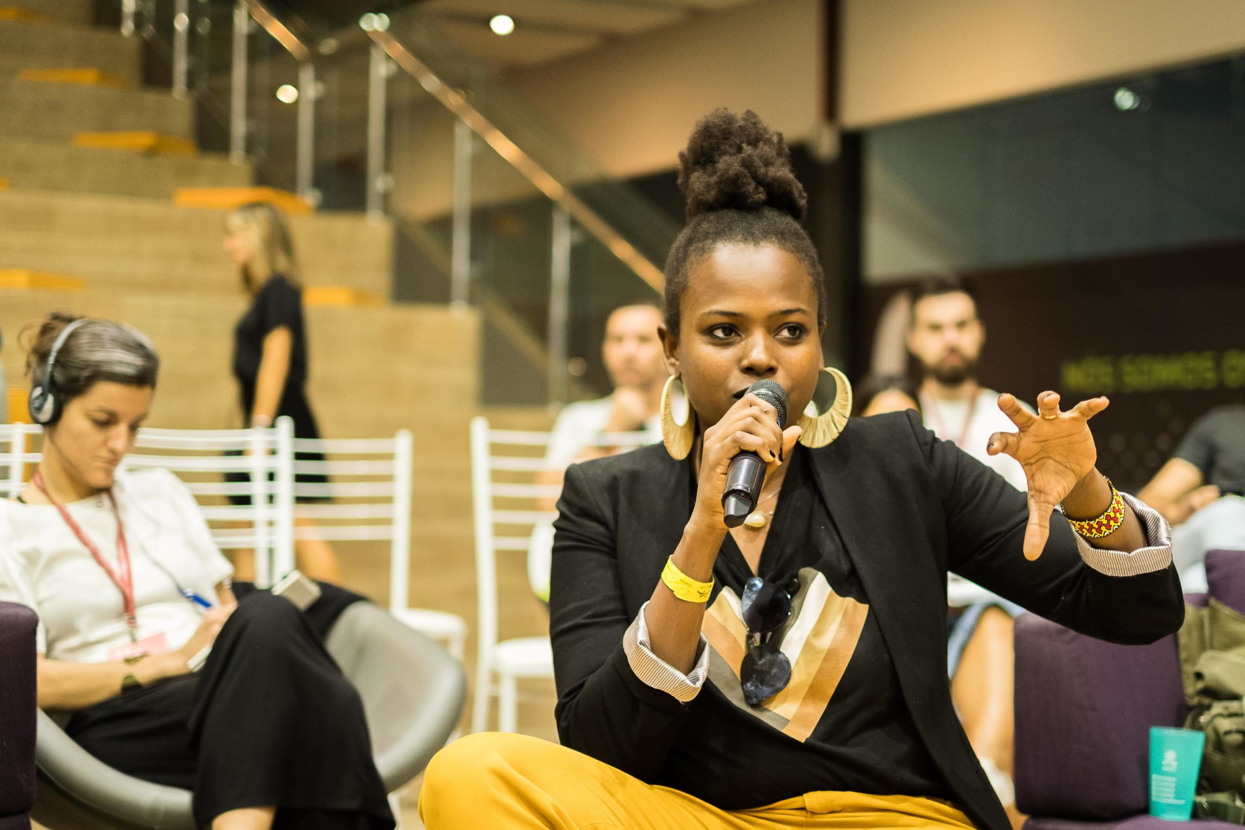 A young black woman holding a microphone addressing a crowd of Impact Hub Makers at a global gathering